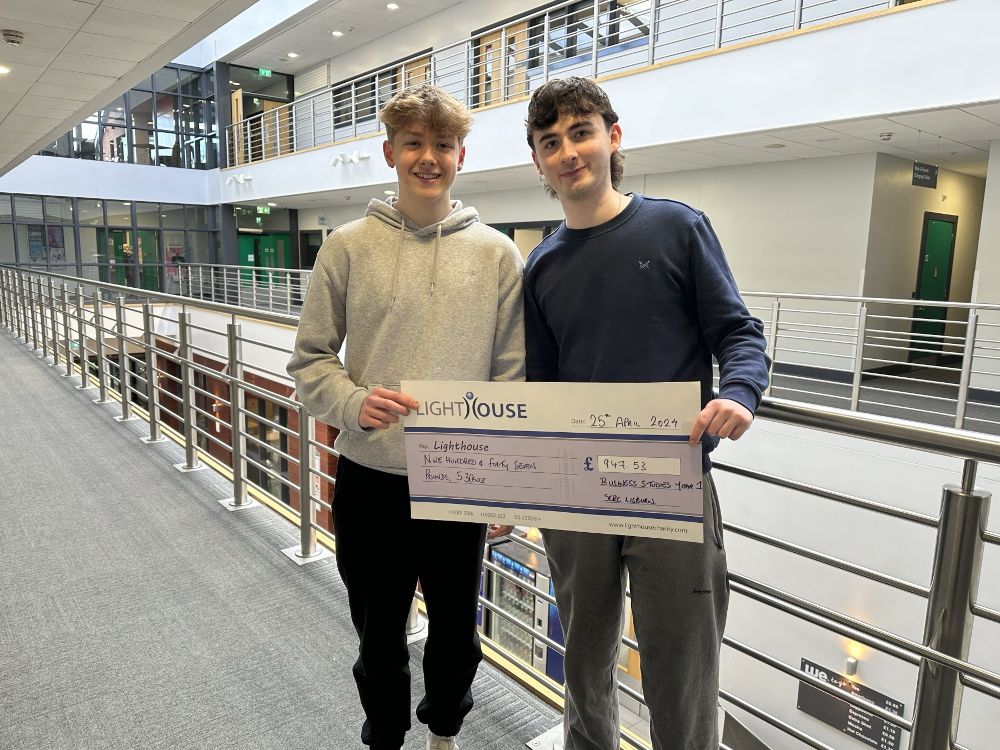 Two students holding a large cheque representing their project to raise charity funds. 